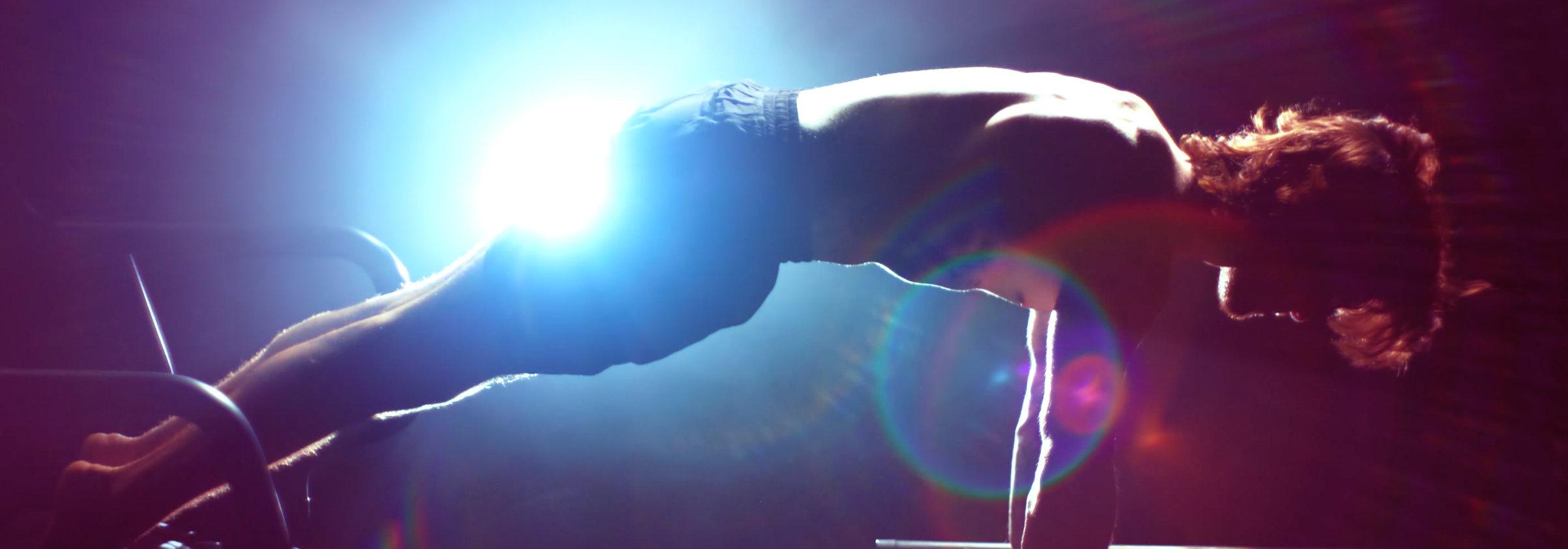 Person leaning over an exercise machine with a bright light source in a dark setting