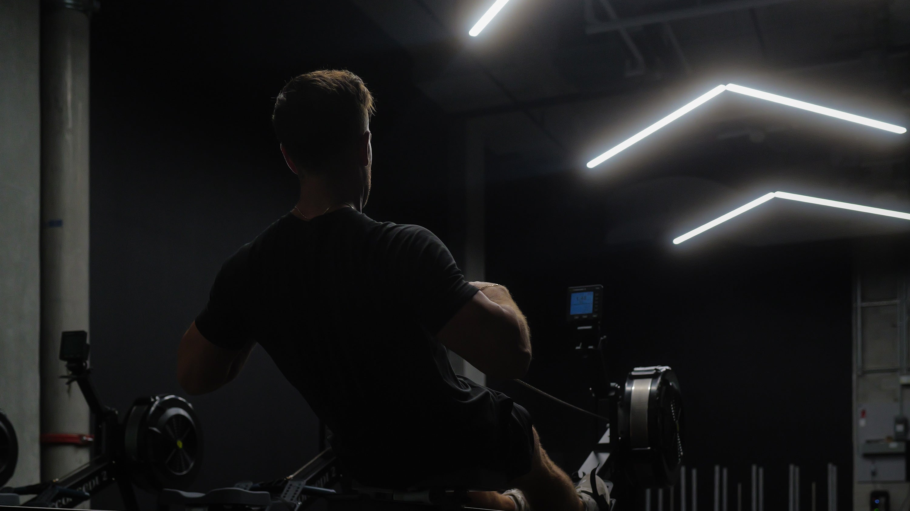 Fitness instructor using a rowing machine in a dimly lit room with neon lights.